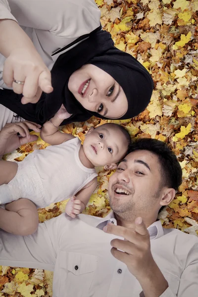 Two parents and their son lying on autumn leaves