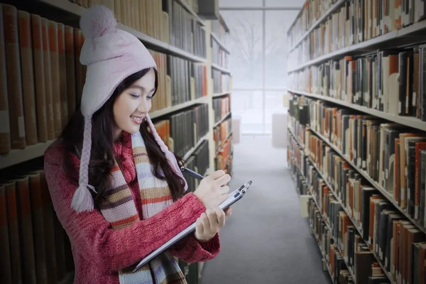 Student writes on clipboard in library