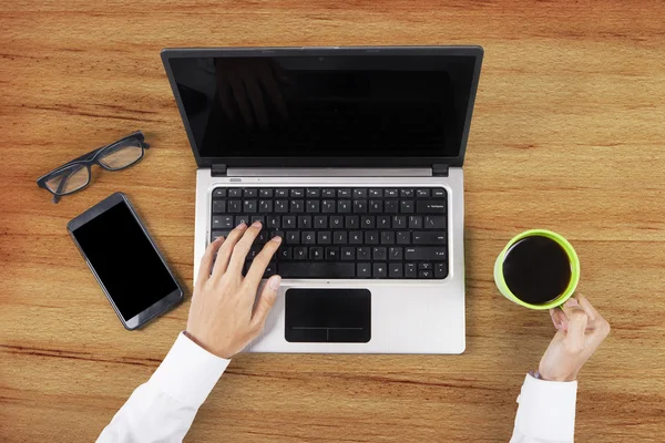 Hands holding coffee and using laptop