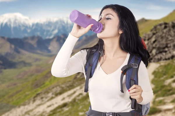 Woman drinks water on the edge of mountain