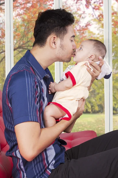 Man sitting on sofa while kissing his baby