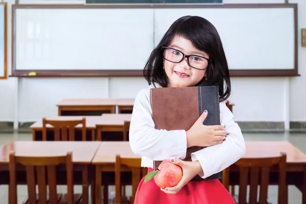 Little learner holds book and apple in class