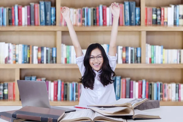 Female student raising hands in library while studying