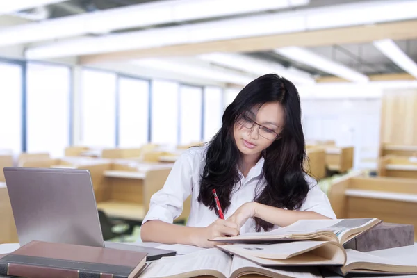 Beautiful female student doing assignment in class