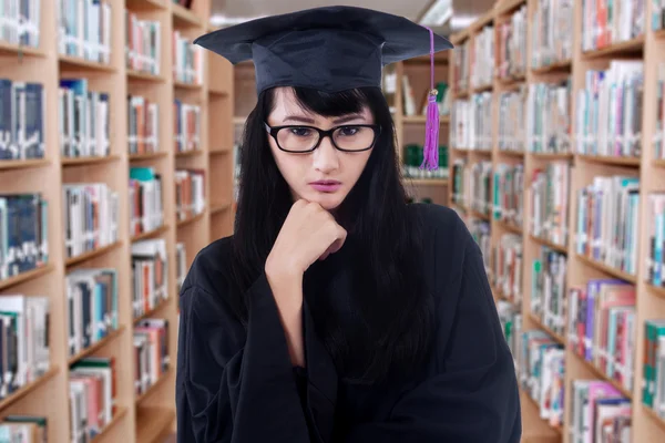 Female bachelor with a graduation cloak in library