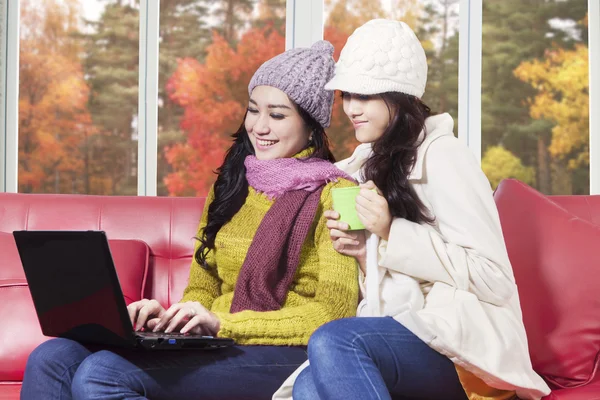 Two women using laptop with autumn background