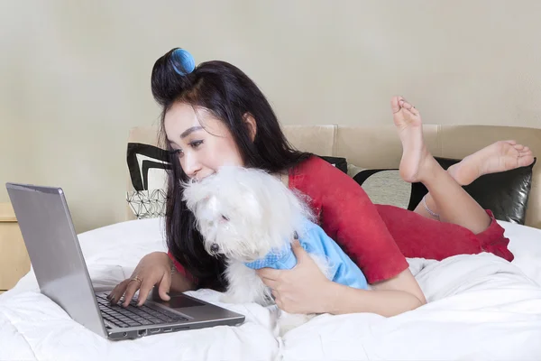 Attractive woman and dog use laptop on bed