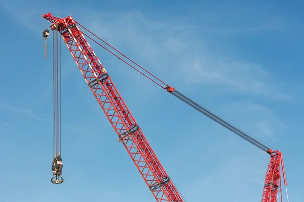 Red crane boom with hook against blu sky