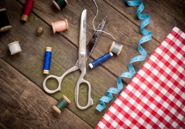 Vintage Background with sewing tools and colored tape. Sewing kit. Scissors, bobbins with thread and needles on the old wooden background