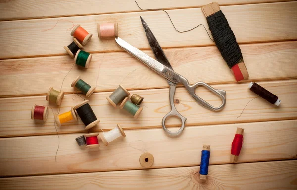 Sewing kit. Scissors, bobbins with thread and needles on the old wooden background