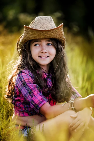 Little girl sitting in a field wearing a cowboy hat