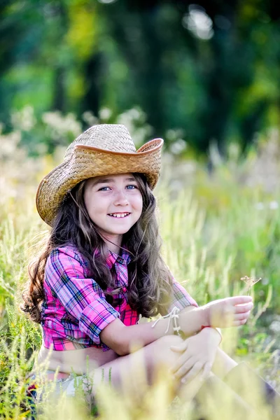 Little girl sitting in a field wearing a cowboy hat