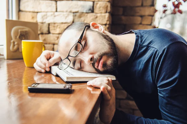 Unshaven man in glasses tired, fell asleep at the table
