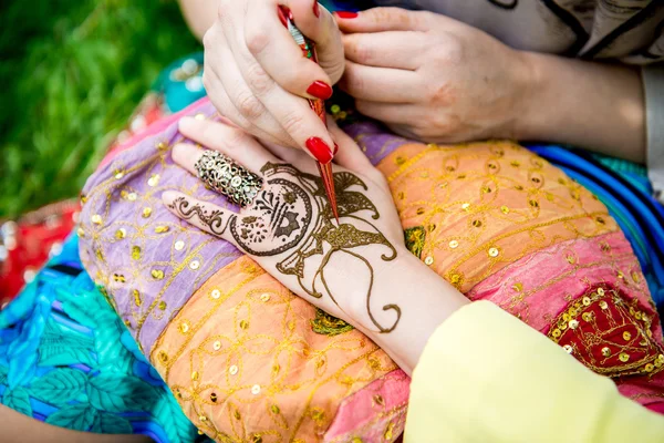 Picture of human hand being decorated with henna tattoo, mehendi