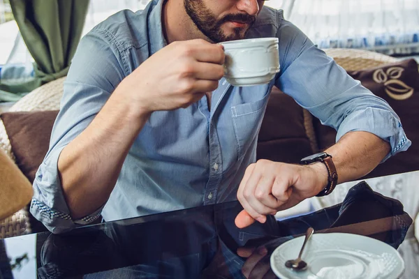 A man sitting in a cafe and looking at his watch and drink coffee