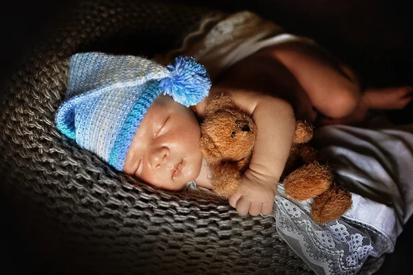 Newborn baby boy asleep wrapped in a blanket close-up, with a bear at hand
