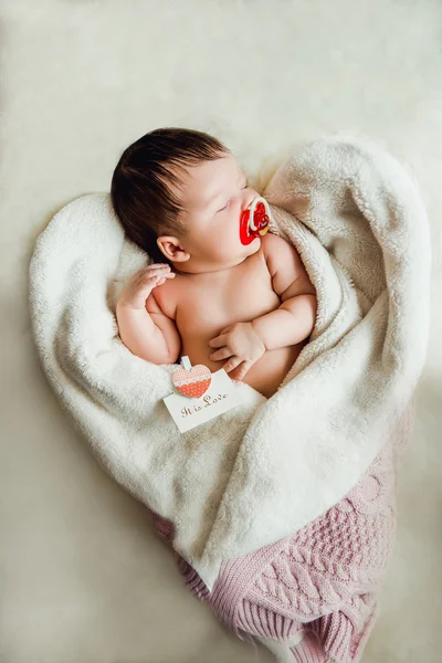 Newborn baby girl sleeps wrapped in white blanket.