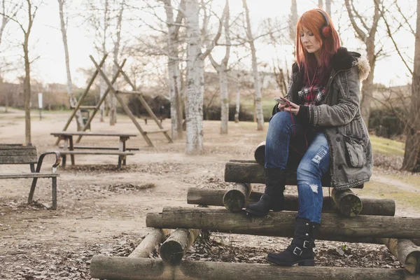 Red-haired girl listening to music in park