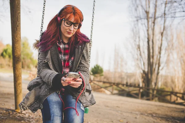 Portrait of girl with red hair listening to music on swings