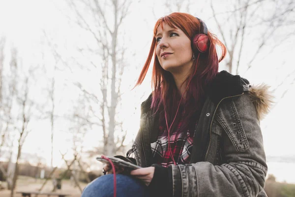 Red-haired girl listening to music in park