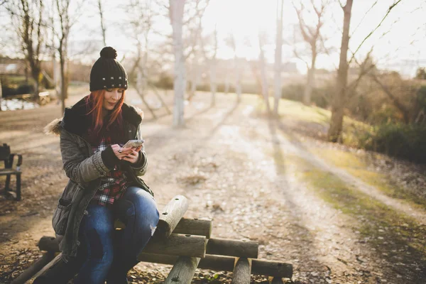 Young red haired woman with her phone on autum scene