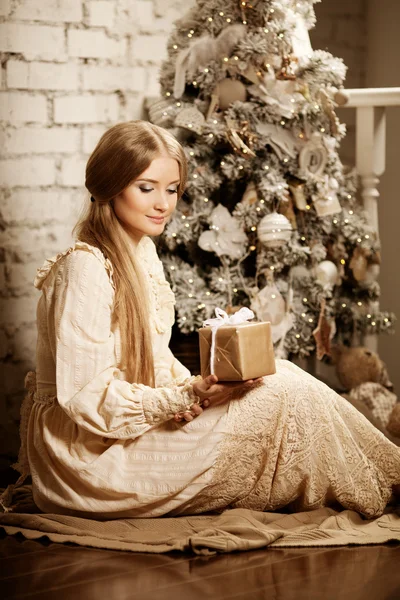 Young luxuy vintage woman near Christmas tree with gift. Beautif