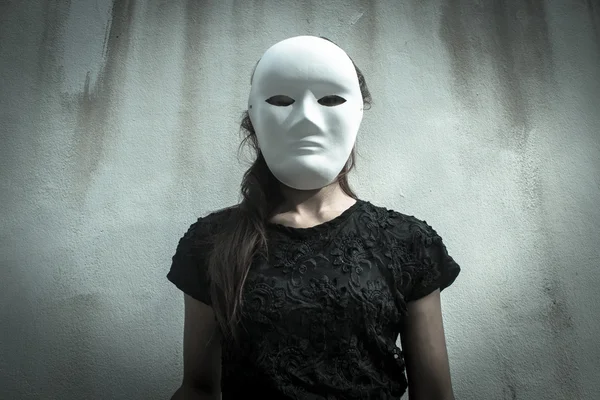 Mysterious woman in black dress wearing white mask