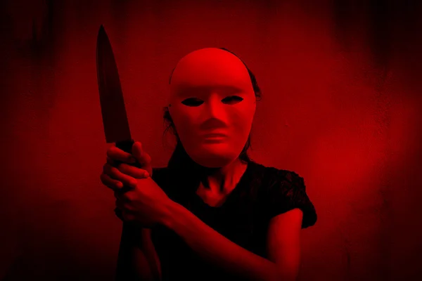 Mysterious woman in black dress wearing white mask with knife