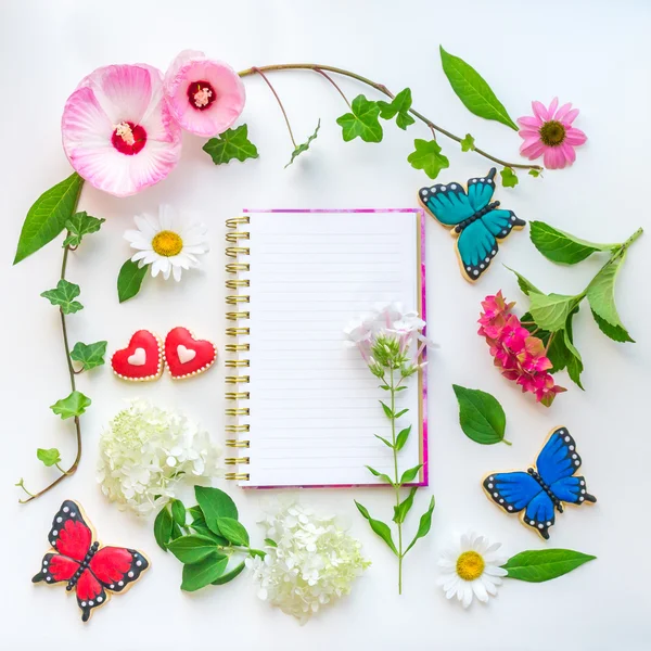 Colorful flowers composition with notebook on light background.  Top view, flat lay.