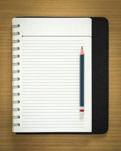 Blank spiral notepad and pencil on wood background