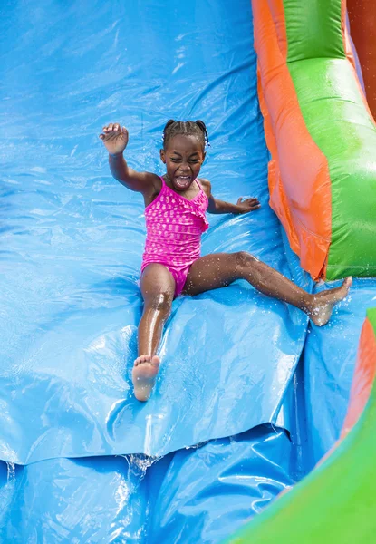 Happy little girl playing outdoors on an inflatable bounce house water slide.