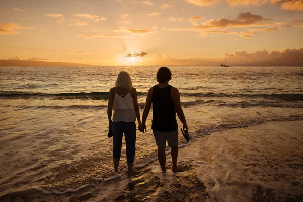 Couple in love walking along the beach barefoot together at sunset. Wide angle photo with lots of copy space