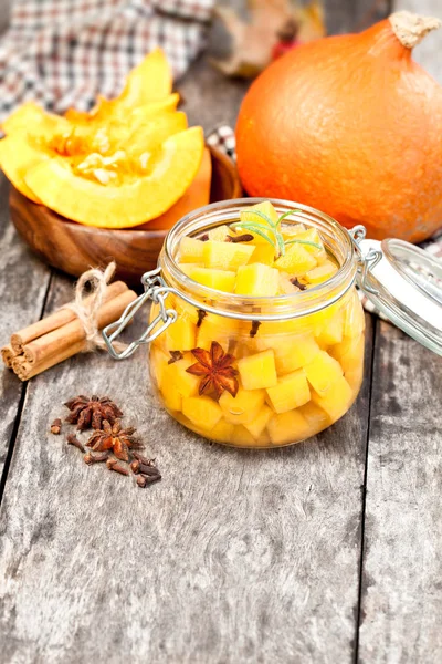 Marinated  pumpkin dices in a glass container on a wooden table.