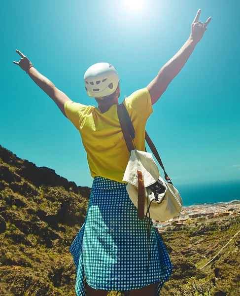 Young happy man in stylish clothes on top of the mountain reaches for the sun and showing rock and roll sign