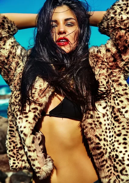 High fashion look.glamor sexy sunbathed Caucasian model girl in leopard fur coat posing behind blue beach ocean water in vogue style