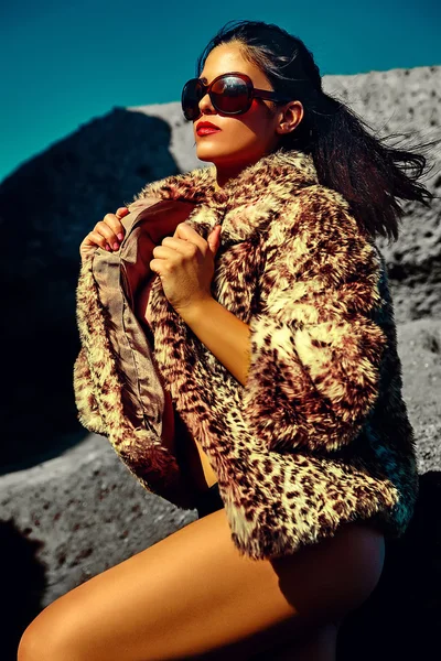 High fashion look.glamor sexy sunbathed Caucasian model girl in leopard fur coat posing outdoors in vogue style