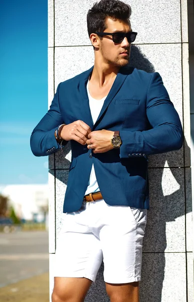 High fashion look.Young stylish confident happy handsome businessman model man in blue suit clothes in the street in sunglasses behind sky