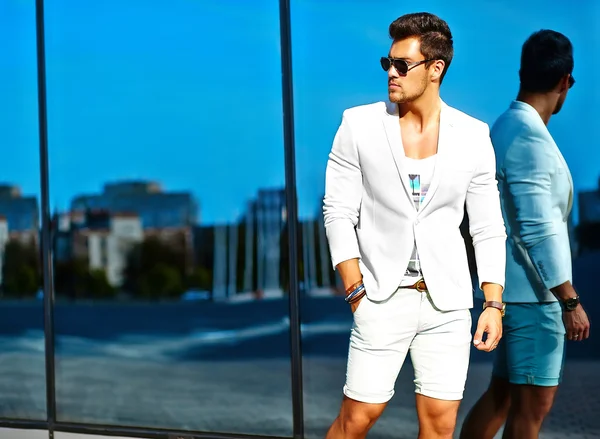 High fashion look.Young stylish confident happy handsome businessman model man in white suit clothes posing and reflecting near mirror