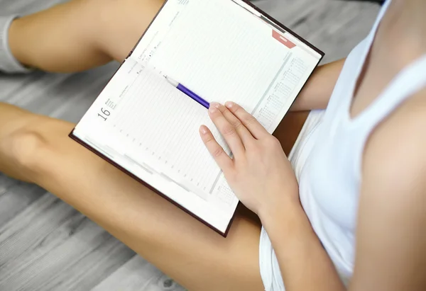 Close up lifestyle portrait of young woman sitting on floor and making notes to her diary