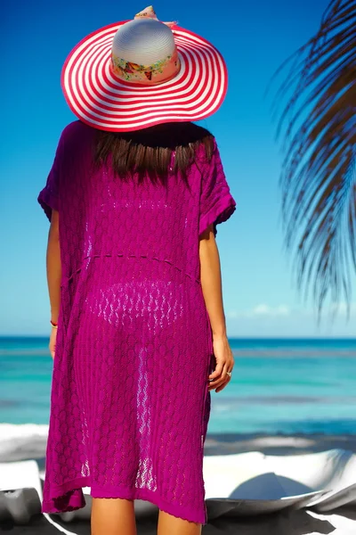 High fashion look. back of glamor sexy model girl  in colorful cloth and sunhat behind blue beach ocean water