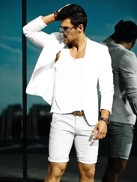 Fashion portrait of young sexy handsome model man in casual white suit in sunglasses in white suit in the street