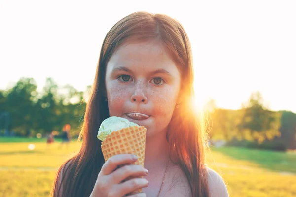 Pretty redhead girl with freckles eating ice cream in sunset lig