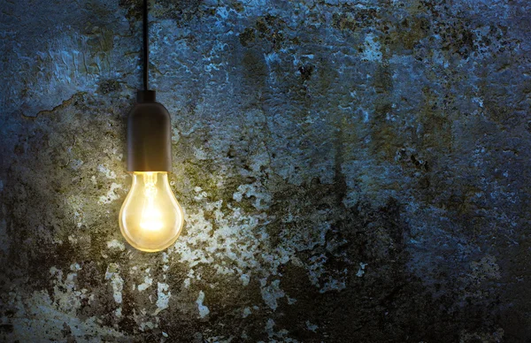 Warm light bulb lamp on grunge wall background in the night