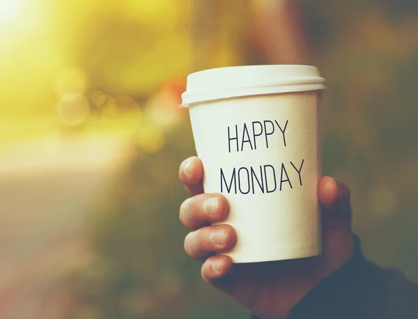 Hand holding paper cup of coffee with Happy Monday text