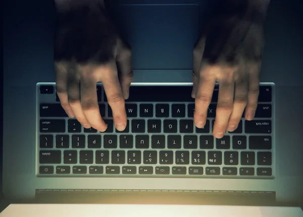Hands with laptop above typing in night