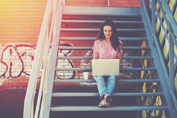 Pretty girl working with laptop sitting on stairs of stairway