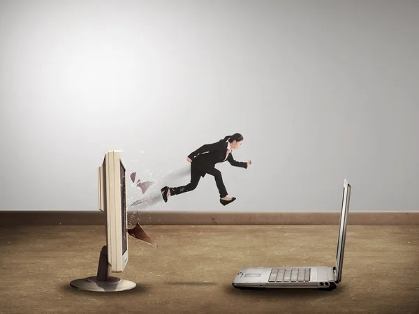 Business woman jumping from desktop computer to laptop