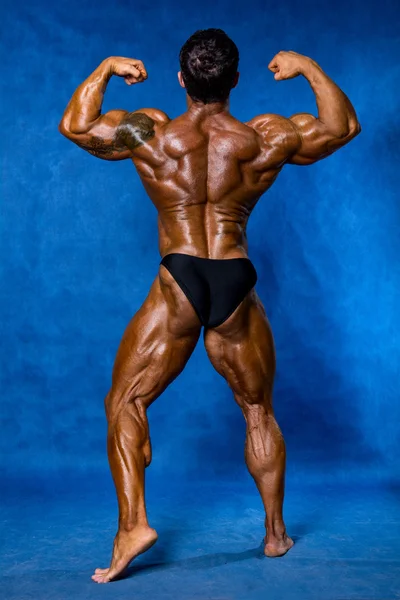 Athletic sports bodybuilder demonstrates posture from the back