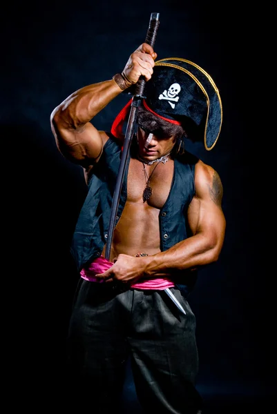 Muscular man in a pirate hat and sword on a black background