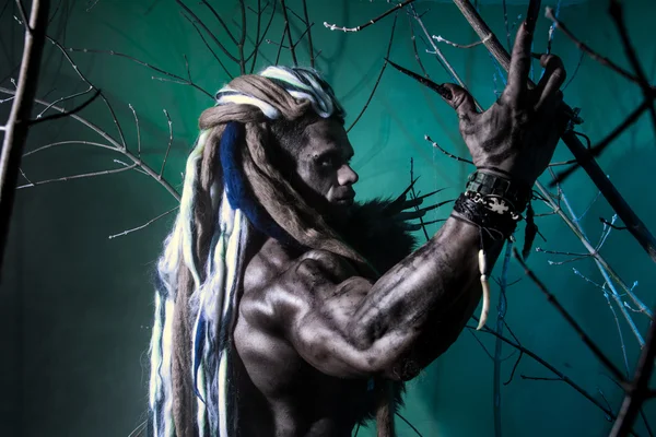 Portrait muscular werewolf with dreadlocks among the branches of